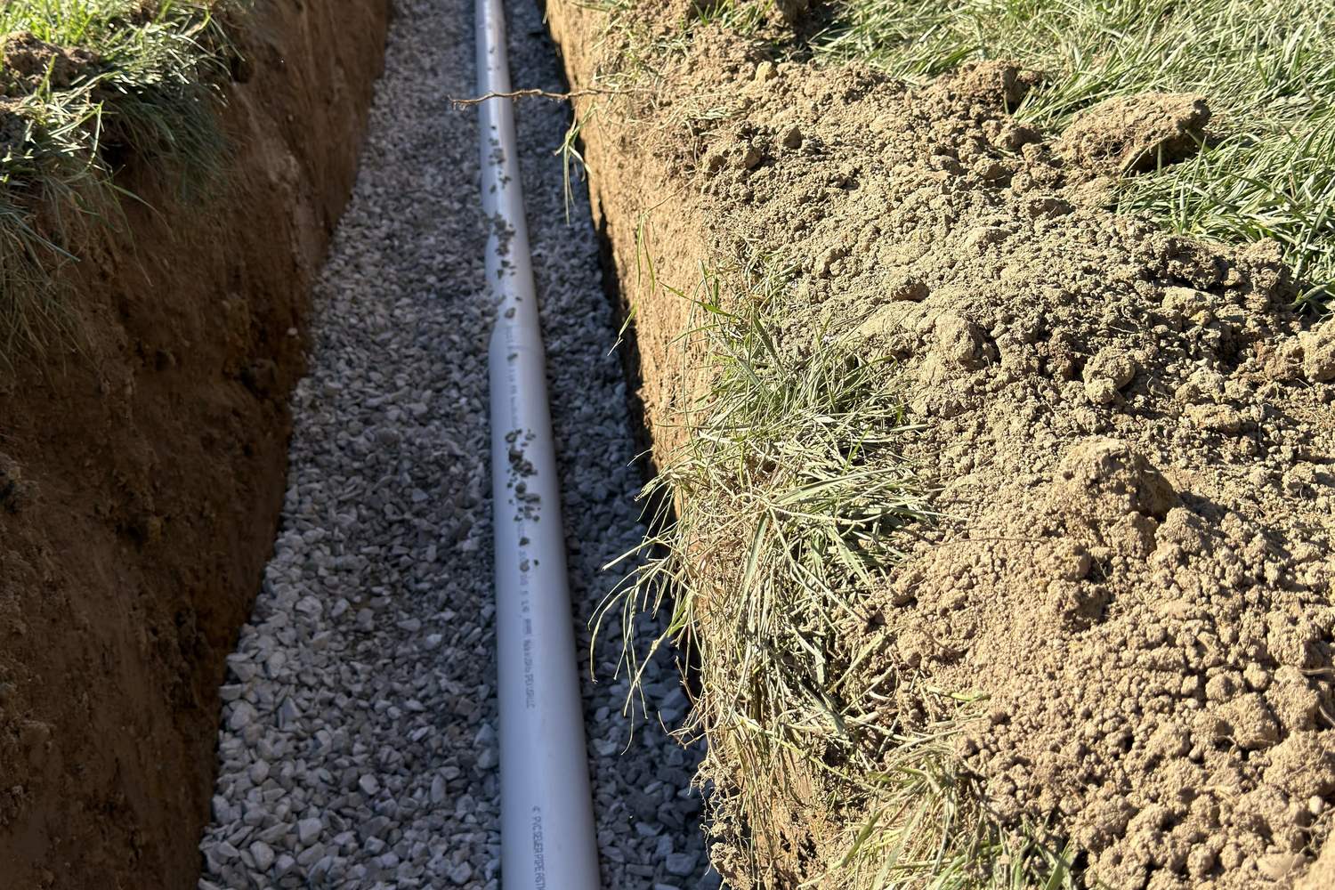 White PVC line bedded on gravel in an open trench before backfill